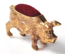 A brass cased pincushion in the form of a pot bellied pig with red velvet cushion to the back.