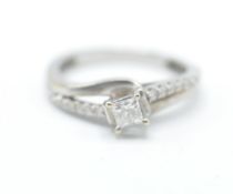 A 9ct white gold crossover ring having a central square cut diamond with white accent stones to