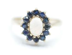 A hallmarked 9ct gold opal and blues stone ring having a central oval opal cabochon with a halo of