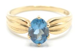 A stamped 375 9ct gold ladies dress ring being set with an oval cut blue stone with pinched reeded