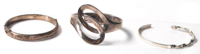 A group of three silver bangle bracelets to include a mid century hinged bangle with engraved floral