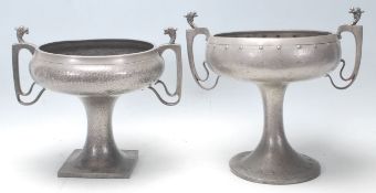 A pair of early 20th Century pewter twin handled vases raised on columnal supports with footed bases