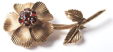 A 9ct gold brooch in the form of a flower being set with six round cut red stones with a hinge to