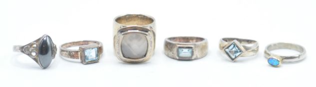 A group of six silver rings to include three rings set with square cut blue stones, a ring set
