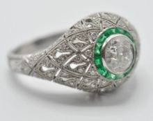 A platinum diamond and emerald ladies dress ring being set with a central round cut diamond with a