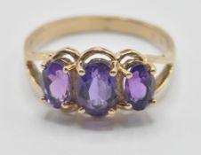 A 9ct gold three stone ring being set with three oval cut purple stones with pierced shoulders. Band