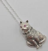 A silver 925 pendant necklace in the form of a sitting cat with red ruby eyes and green sones to the
