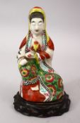 A 19TH CENTURY CHINESE FAMILLE ROSE PORCELAIN FIGURE OF GUANYIN, seated upon a carved hardwood base,