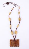 A CHINESE CARVED JADE OR HARD STONE PENDANT & BEADS, all attached as part of a necklace, with carved