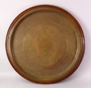 A LARGE ISLAMIC BRASS CIRCULAR TRAY WITH HARDWOOD MOUNT, WITH KUFIC CALLIGRAPHY, 77cm.