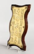 AN EARLY 20TH CENTURY BRASS AND OAK CRIBBAGE BOARD, of serpentine outline. 11ins x 5.5ins.