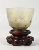 A GOOD JADE CUP on a wooden stand. 2.5ins diameter.