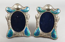 A PAIR OF OVAL SILVER AND ENAMEL UPRIGHT PHOTOGRAPH FRAMES. 8ins x 5ins.