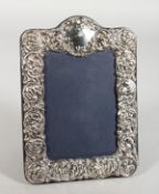 A SILVER PHOTOGRAPH FRAME repousse scrolls and flowers. 8ins x 6ins.