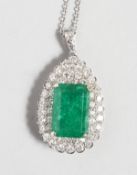A GOOD 18CT WHITE GOLD PEAR SHAPED PENDANT inset with a central rectangular emerald, surrounded by