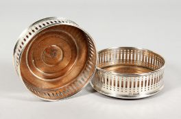 A PAIR OF PIERCED SILVER WINE COASTERS with turned wood bases. 4ins diameter. London 1973.