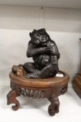 A Japanese style cast metal model of a monkey seated on a hardwood stand.
