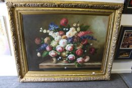 A large and impressive still life of flowers in an urn on a ledge, in a decorative gilt frame.