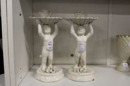 A pair of continental white porcelain candlesticks modelled as cherubs holding aloft a shell.