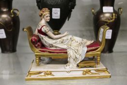 A continental porcelain model of a young lady reclining on a day bed.