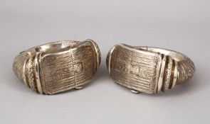A GOOD PAIR OF ISLAMIC SILVER COATED LOCKING BANGLES, each carved decoration of hanging motifs, 11cm