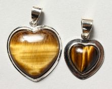 TWO SILVER AND TIGERS EYE HEART SHAPED PENDANTS.