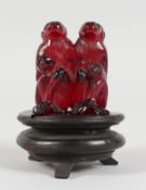 A GOOD CARVED AMBER GROUP OF TWO MONKEYS, 2ins high, on a carved wooden stand.