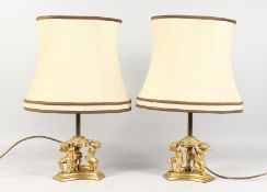 A GOOD PAIR OF ORMOLU TABLE LAMPS, the concave sided base with three kneeling figures. 13ins high.