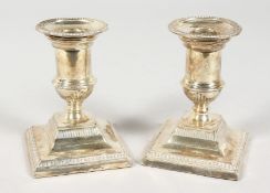 A SMALL PAIR OF SILVER CANDLESTICKS on square bases. 4ins high. Sheffield 1902.