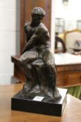 A seated male nude on a square marble base.