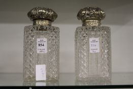 A pair of cut glass square shaped decanters with hinged embossed silver tops (one lacking stopper