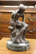 A cast bronze of a seated female nude on a circular marble base.