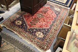 A Persian rug, red ground, the central panel with stylized tree and bird motifs.