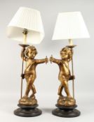 A GOOD PAIR OF ITALIAN CARVED WOOD AND GILDED CHERUB LAMPS AND SHADES on circular bases. 27ins