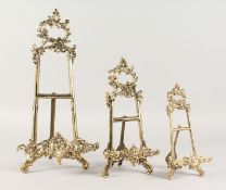 A SET OF THREE BRASS EASELS. 16ins, 11ins and 9ins high.