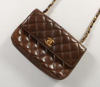A GOOD CHANEL BROWN LEATHER PADDED PURSE with leather and gilt long handle. 7ins long, in a black