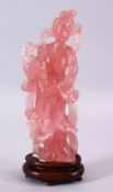 A CHINESE CARVED ROSE QUARTZ FIGURE OF GUANYIN, stood holding a bouquet of flora, on a carved wooden