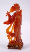 A CHINESE CARVED AGATE FIGURE OF GUANYIN, holding a fan and robes, on a carved wooden base, 19cm
