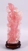 A CHINESE CARVED ROSE QUARTZ FIGURE OF GUANYIN, stood holding a bouquet of flora, on a carved wooden