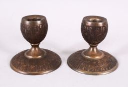 A GOOD PAIR OF ISLAMIC QAJAR WHITE METAL CANDLESTICKS, carved with figures in fez, 9cm diameter x