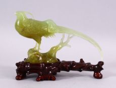 A CHINESE CARVED JADE MODEL OF A PEACOCK, stood upon stylized wooden outcrop, on a carved hardwood