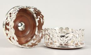 A PAIR OF SILVER PLATE CHERUB DESIGN WINE COASTERS with turned wood bases. 5ins diameter.