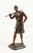 A SMALL BRONZE FIGURE of a standing Arab man holding a stick on his shoulder. 12.5ins high.