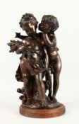 A BRONZE GROUP, depicting a young boy whispering to a young girl, on a wooden base. 17ins high.
