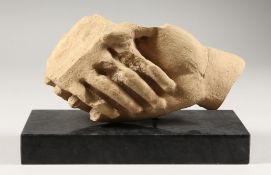 A POTTERY SCULPTURE OF CLASPED HANDS, on a marble base. 9ins long.