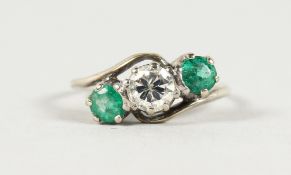 A THREE STONE EMERALD AND DIAMOND RING in white gold.