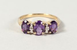 A 9CT GOLD THREE STONE OVAL AMETHYST AND DIAMOND RING.