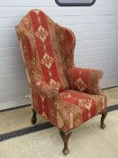 A large and impressive Georgian style wing back open armchair raised over substantial mahogany legs