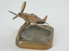 A brass smokers receptacle having Spitfire model over with rotating propeller, 15cm wingspan.