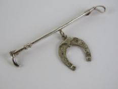 A silver stock pin or brooch in the form of a riding crop with horse shoe under, marked sil,